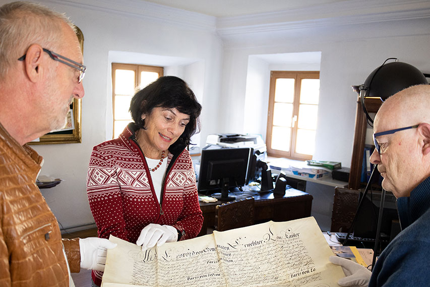 Zwei Männer und eine Frau betrachten eine historische Urkunde, die sie mit weißen Handschuhen anfassen.